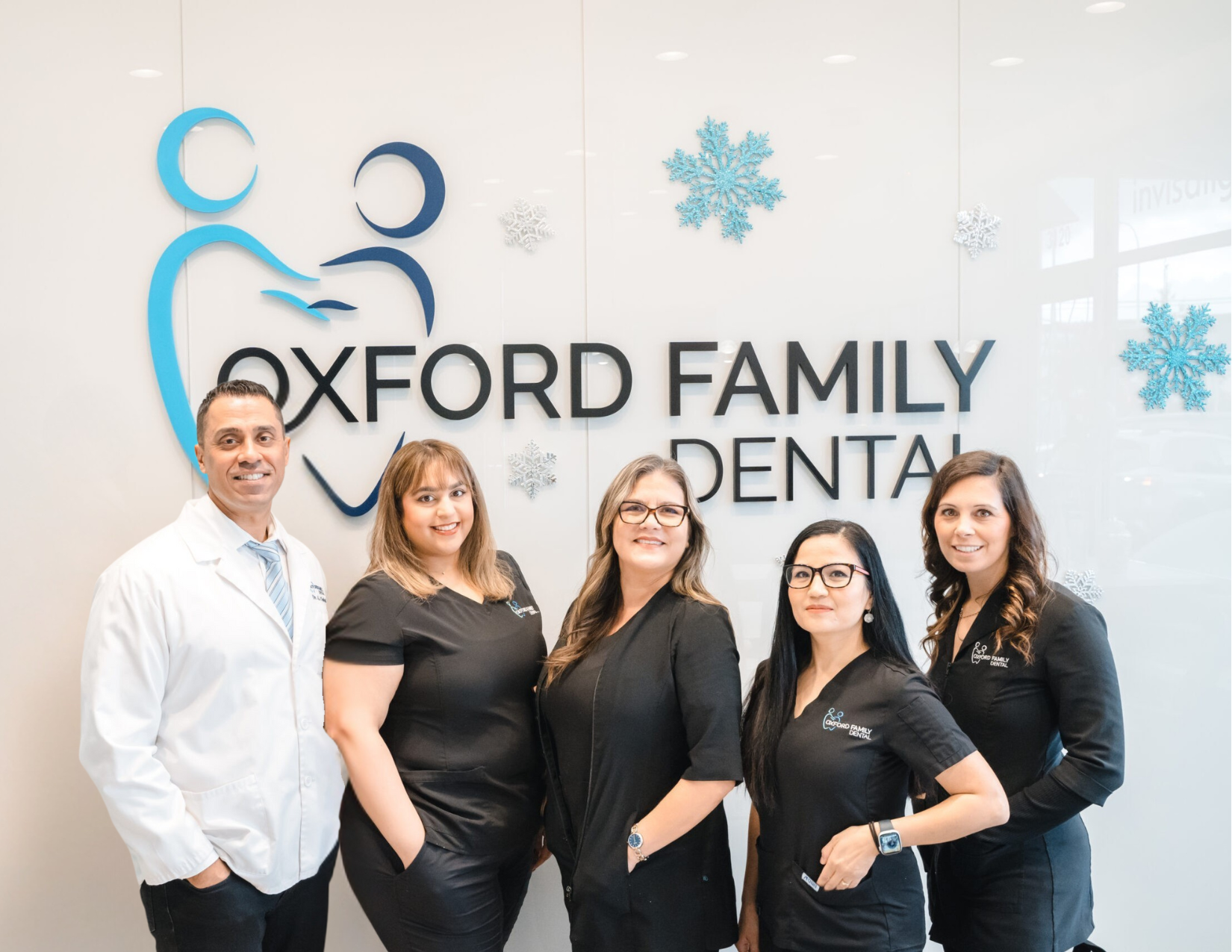 Dr. Chahal and the Oxford Family Dental team in front of the office logo wall